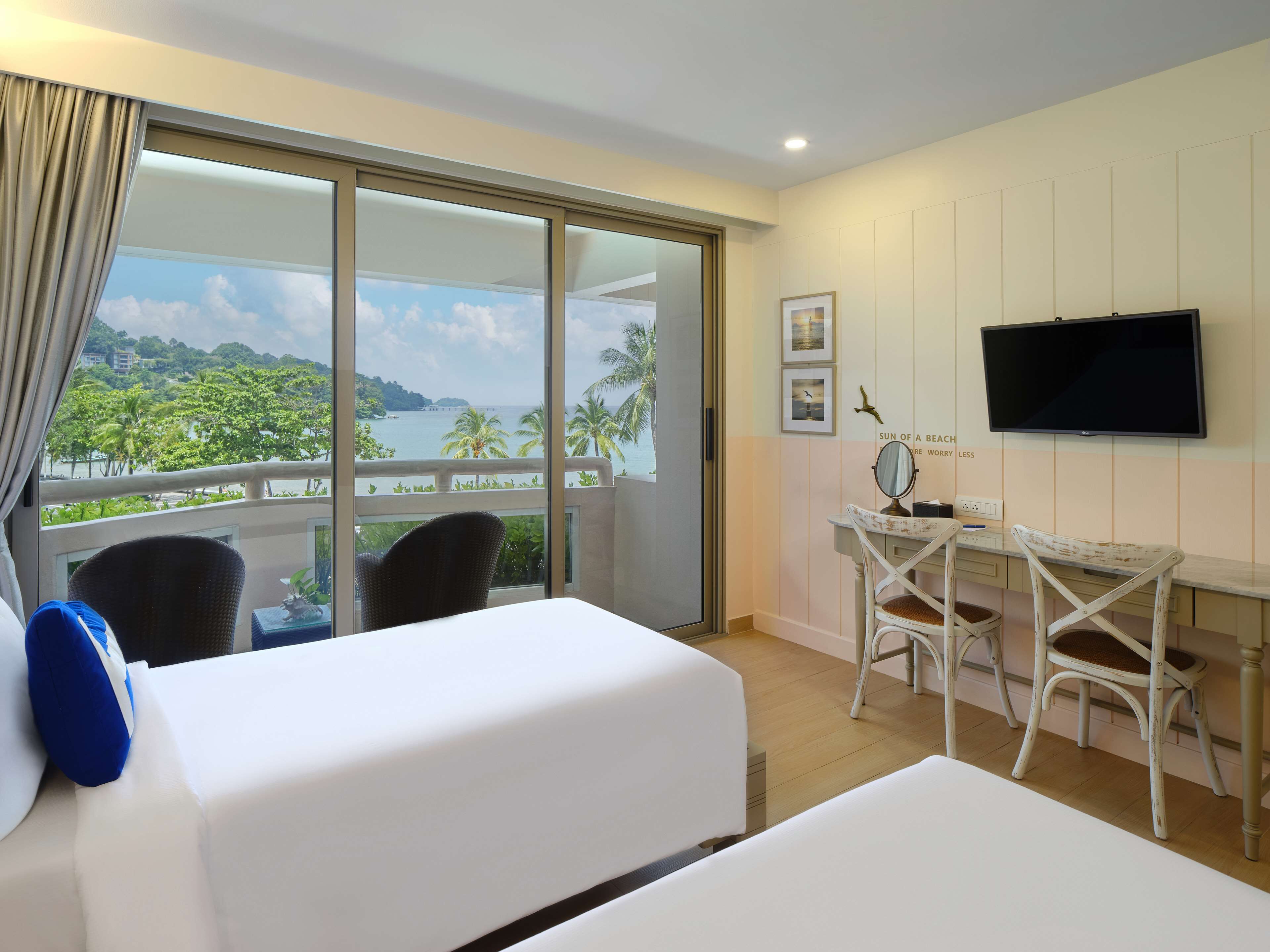 A hotel room with a large balcony, a TV, a desk with a chair, and two beds.