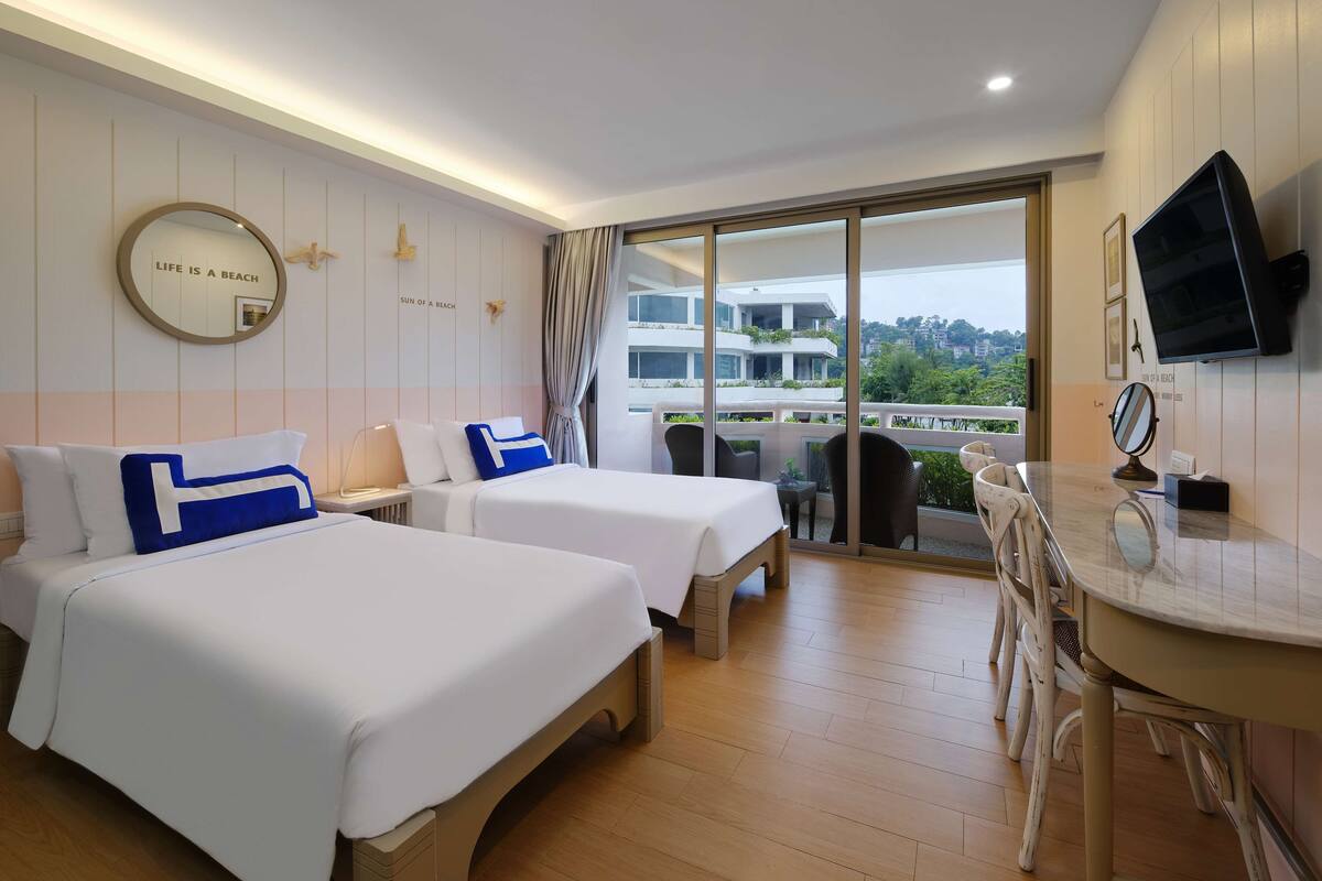 Habitación de hotel con dos camas, balcón con vistas, televisor y escritorio con silla.