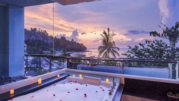 A bathtub with rose petals and candles, overlooking a beach and sunset.
