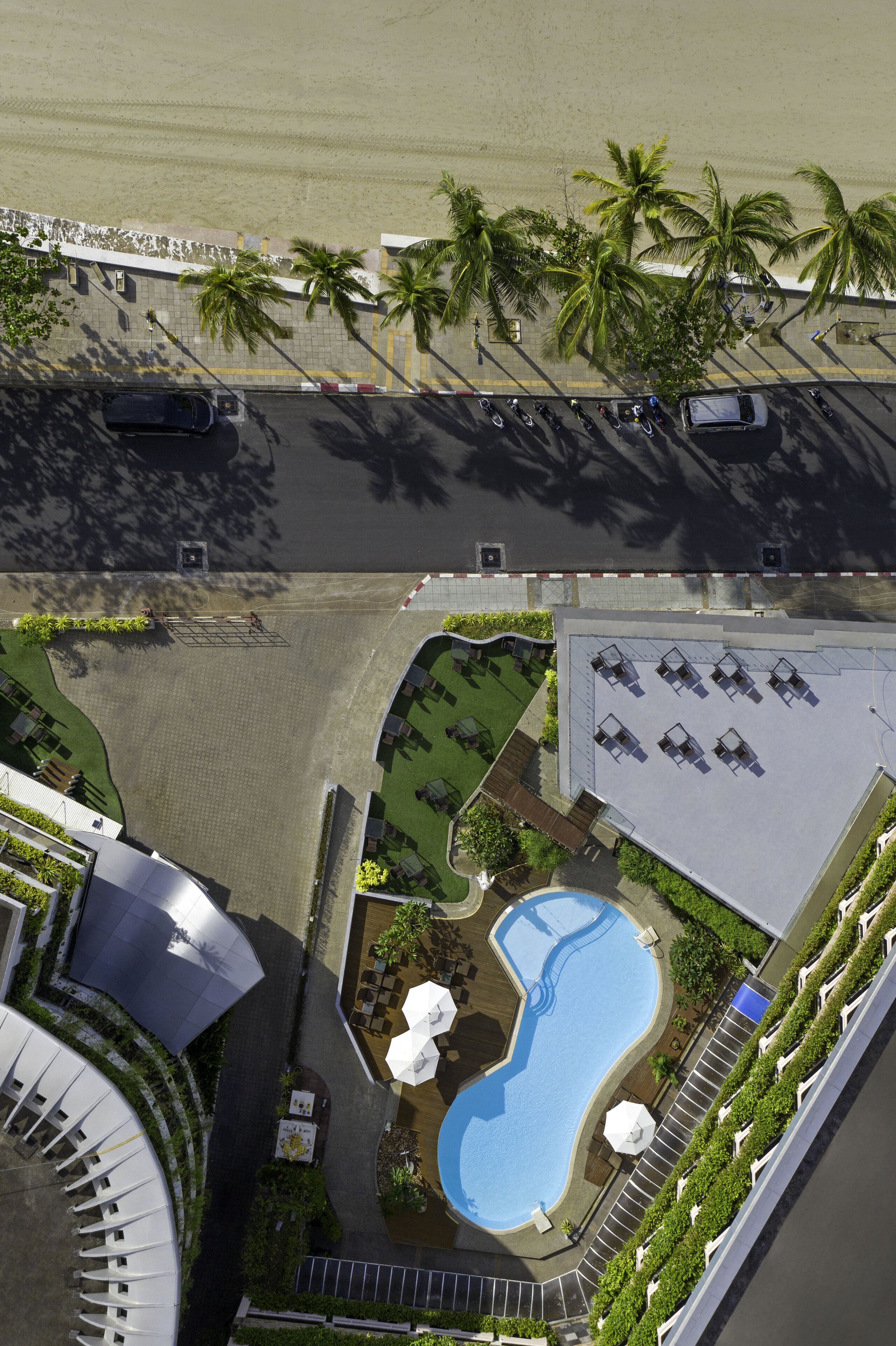 Vista aérea de un hotel con piscina, palmeras y zona de estacionamiento.