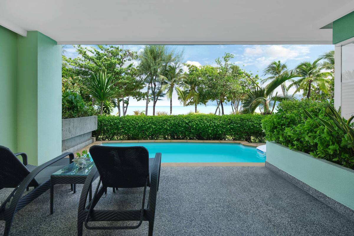Un espacio al aire libre techado con piscina, mobiliario y vistas al océano y palmeras.