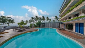 A swimming pool with lounge chairs, palm trees, and a view of the sea.