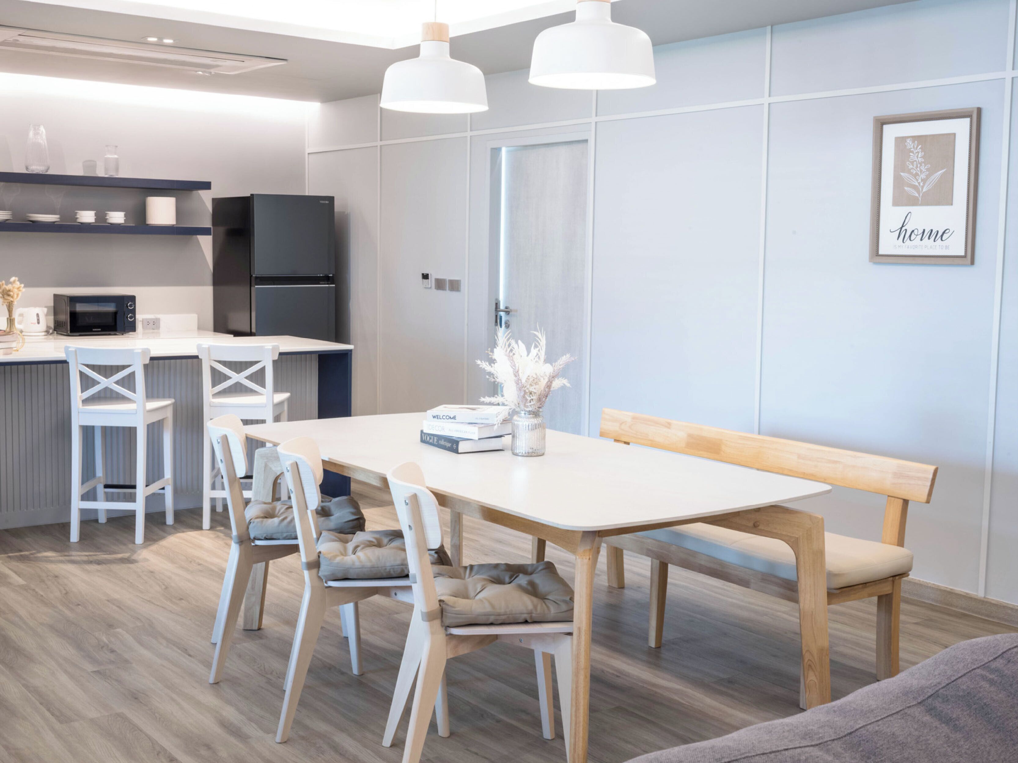 A modern kitchen with white appliances, a dining area with a wooden bench and chairs, and a wall-mounted light fixture.