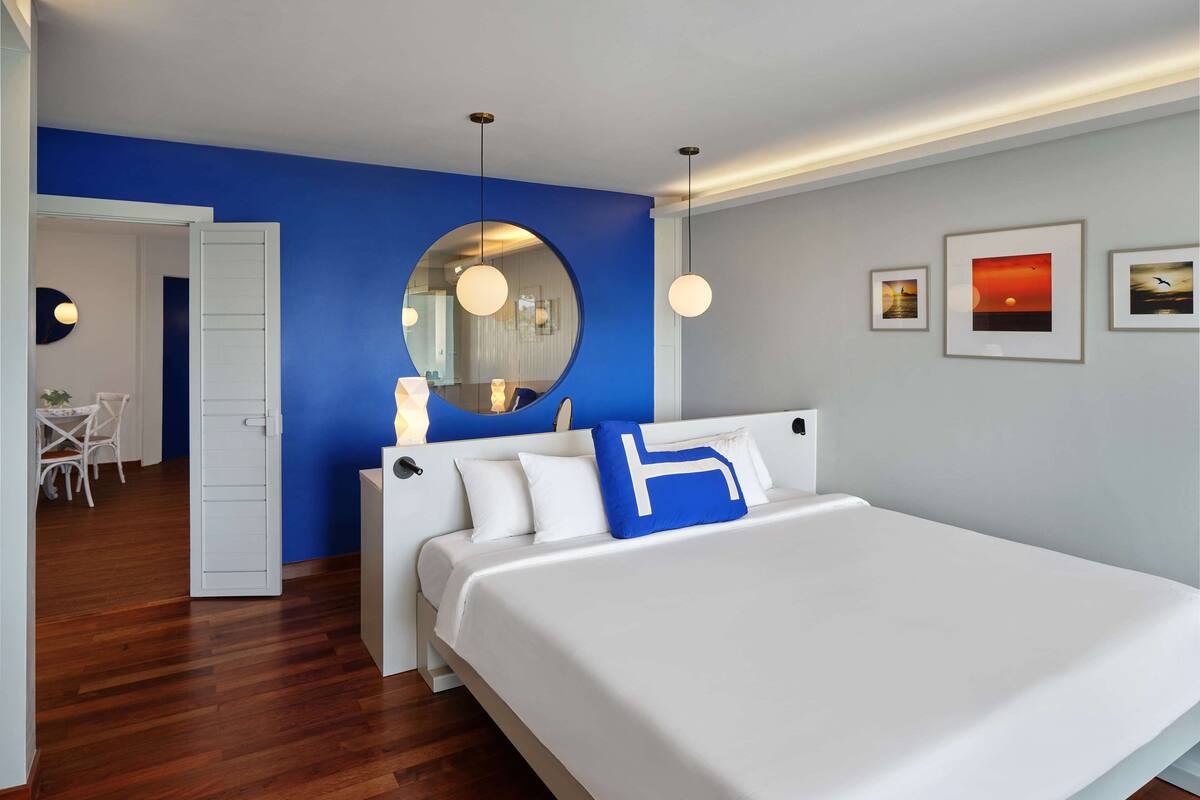 Un dormitorio moderno con una cama grande, un espejo redondo y una zona de comedor con mesa y sillas.