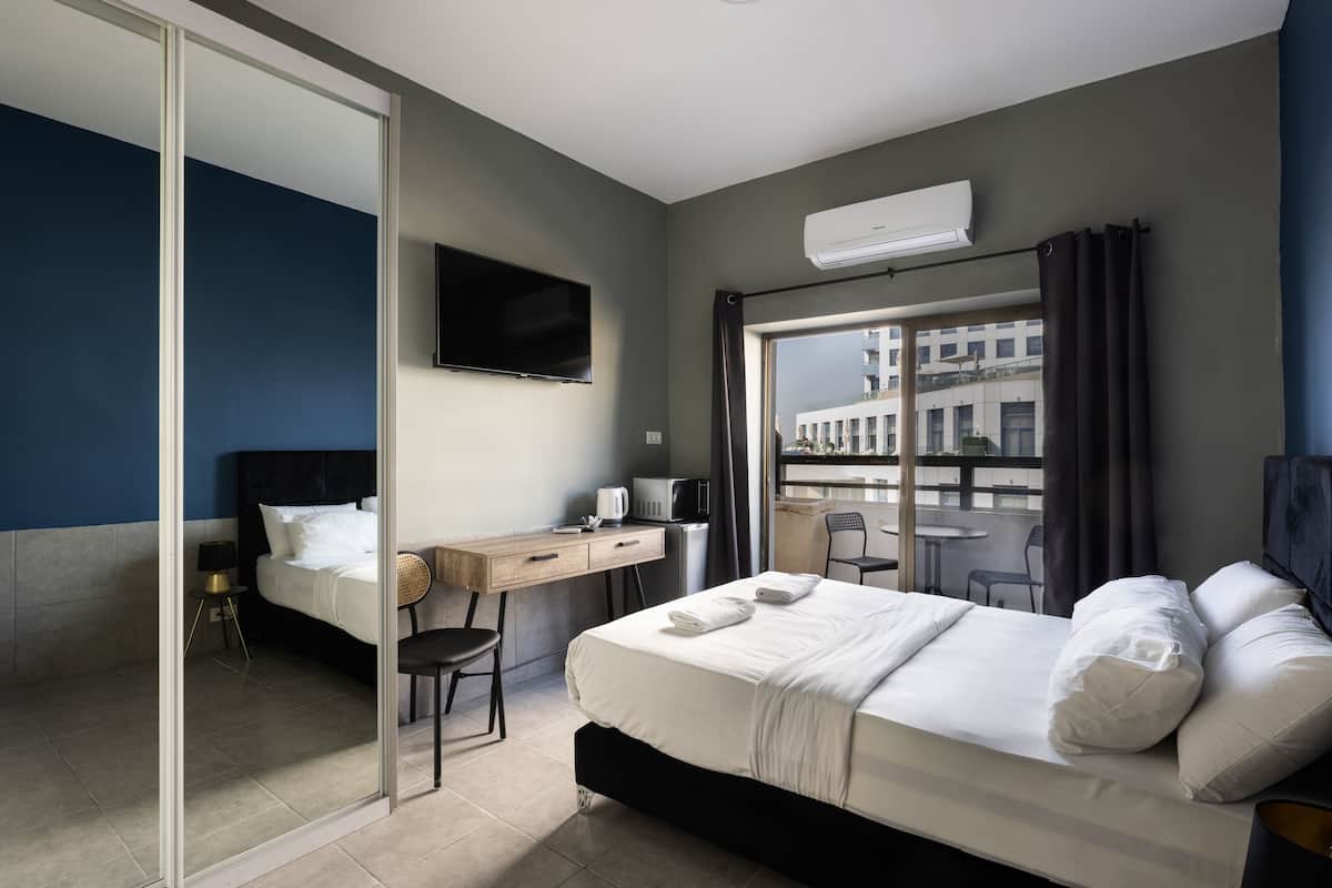 A modern hotel room with a bed, desk, and a large window offering a view of the city.