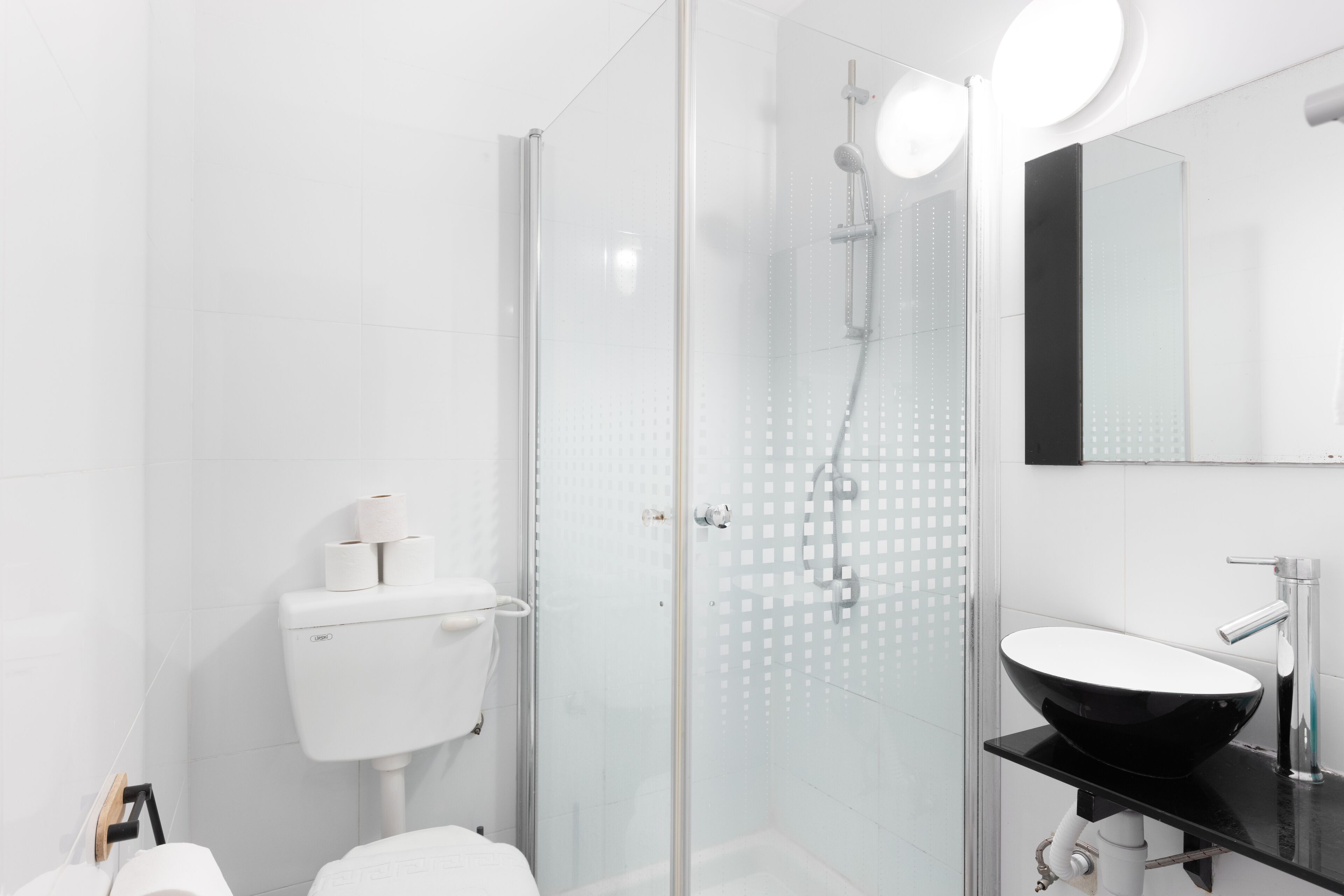 Un bagno moderno con doccia vetrata, un water bianco e un lavandino nero con uno specchio sopra.