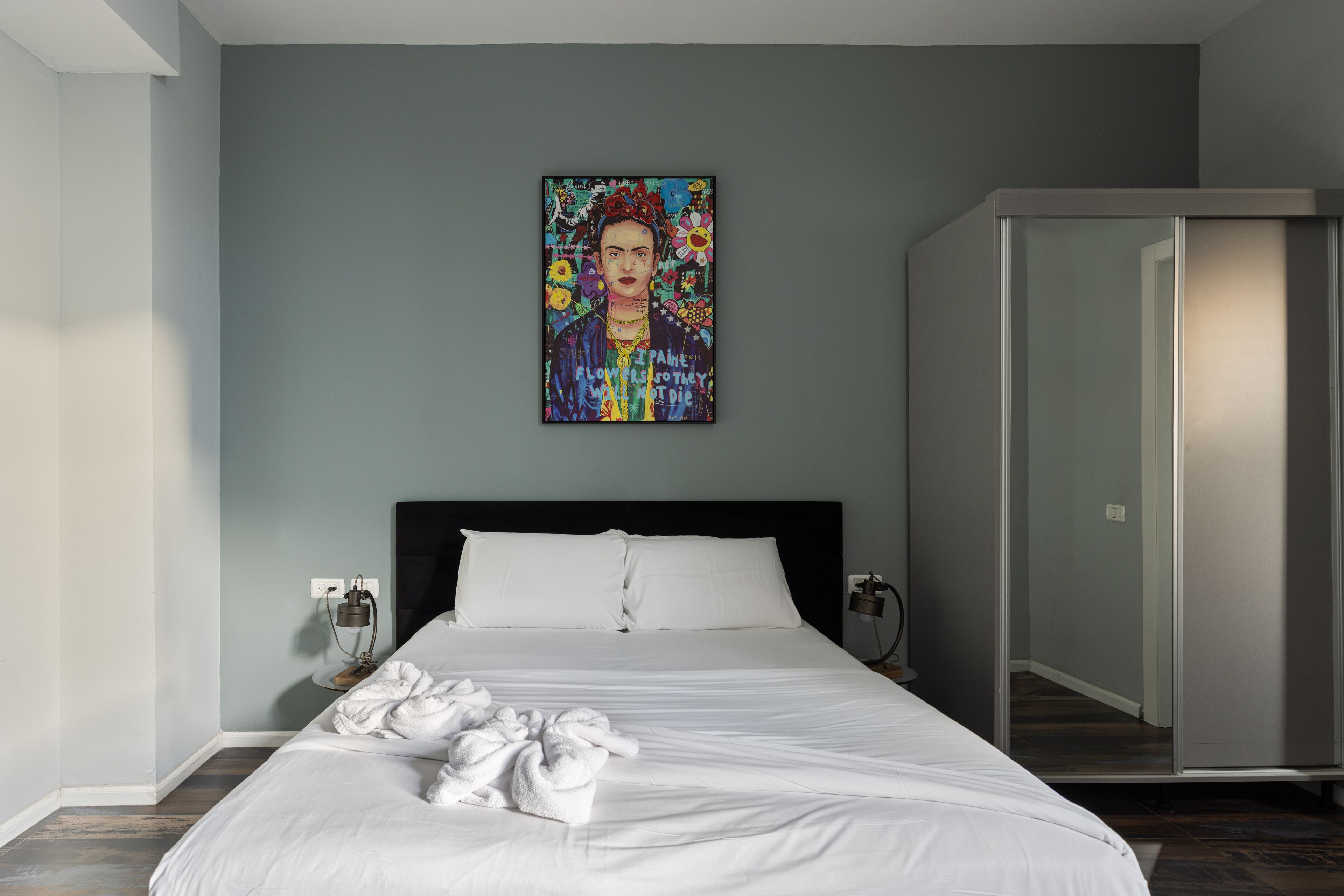 A modern bedroom with a large bed, a bedside table, a wall-mounted painting, and a wardrobe.