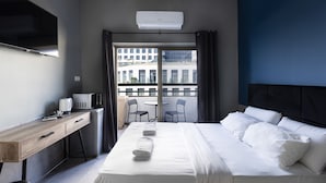 Una camera d'albergo moderna con un letto, una scrivania, una televisione e un balcone con sedie.