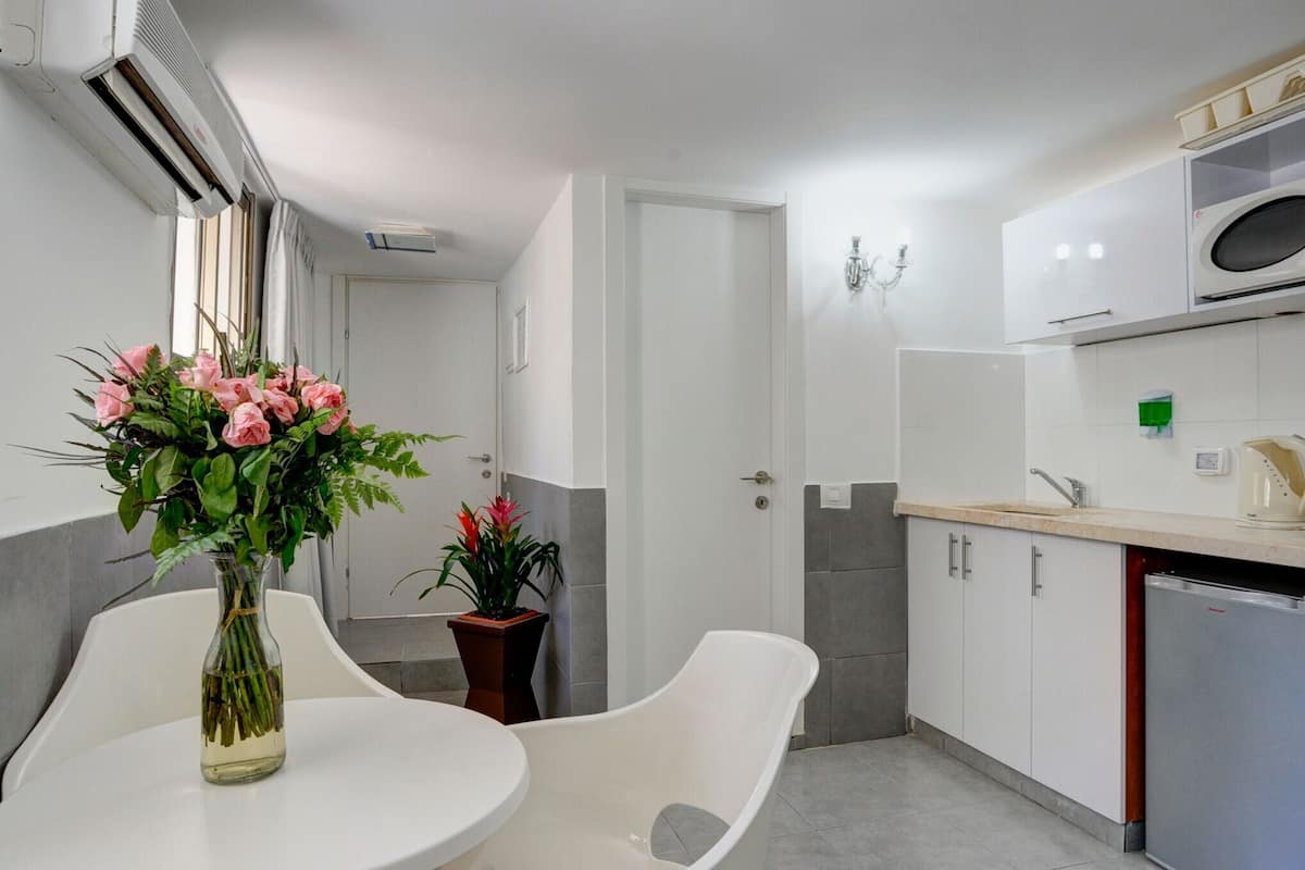 A modern kitchen with white cabinets, a built-in microwave, and a refrigerator. There is a white dining table with chairs, and a vase with flowers on it.