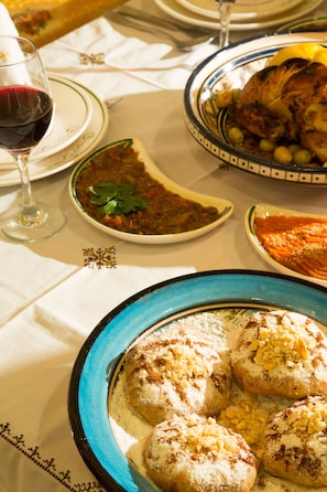 A dining table with various dishes, including a plate of pastries, a bowl of soup, and a roasted chicken. - Dar El Kébira (Rabat)