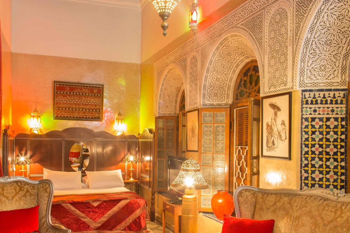 A traditional Moroccan interior with a bed, sofas, a coffee table, and ornate wall decorations.