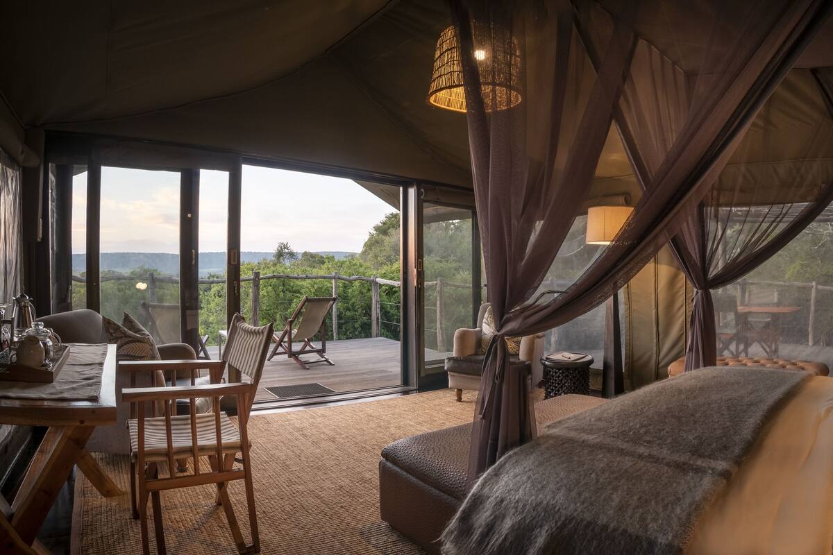A cozy room with a large bed, a wooden table with chairs, and a view of the outdoors.
