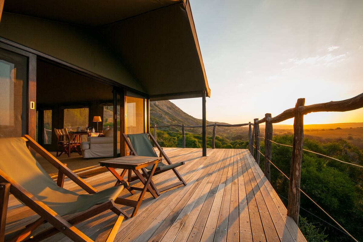 A wooden deck with lounge chairs and a table, overlooking a mountainous landscape.