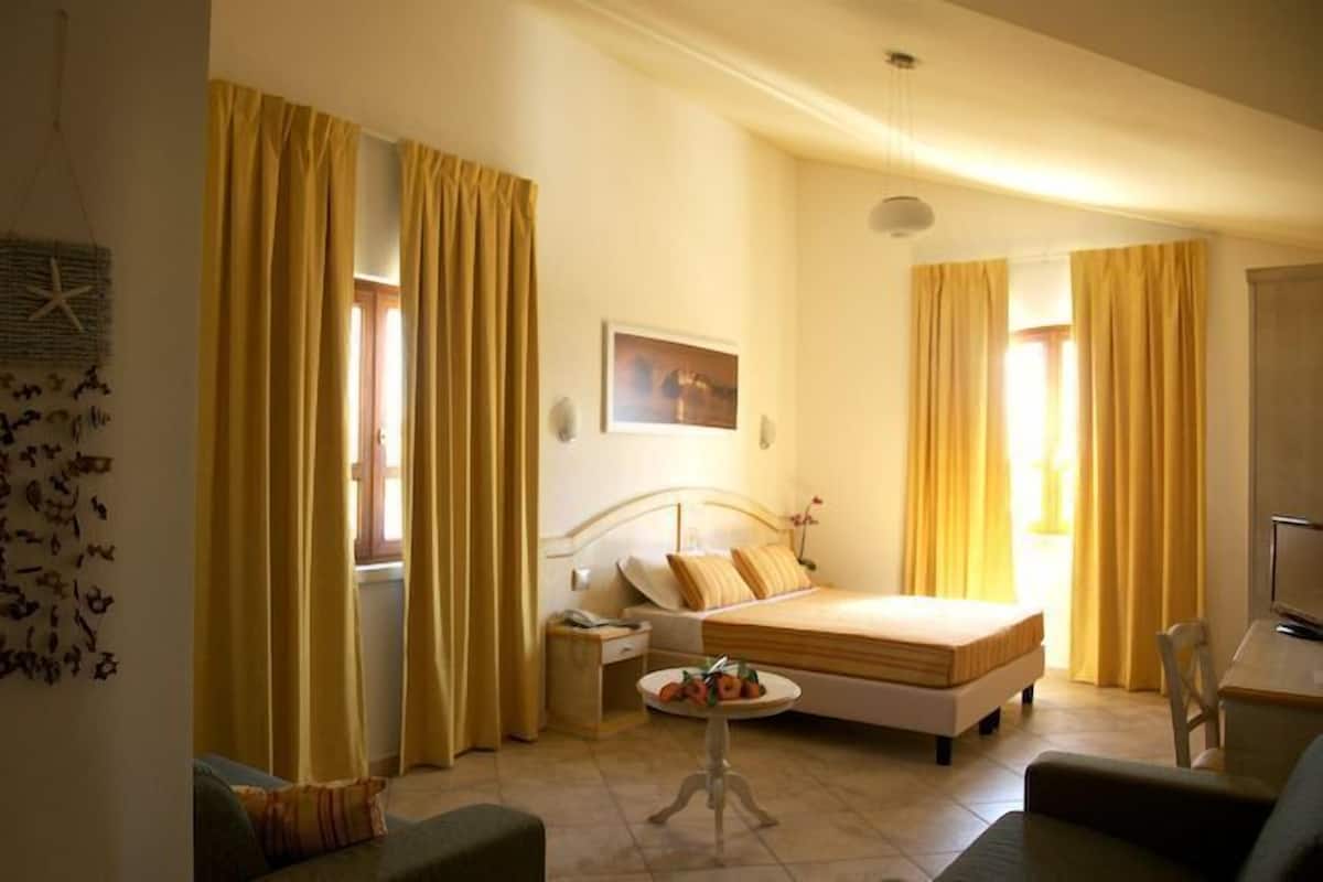 A hotel room with a bed, a bedside table, a chair, and a small table with a plant.