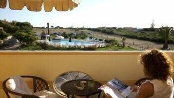 A balcony with a view of a swimming pool, chairs, and a table.