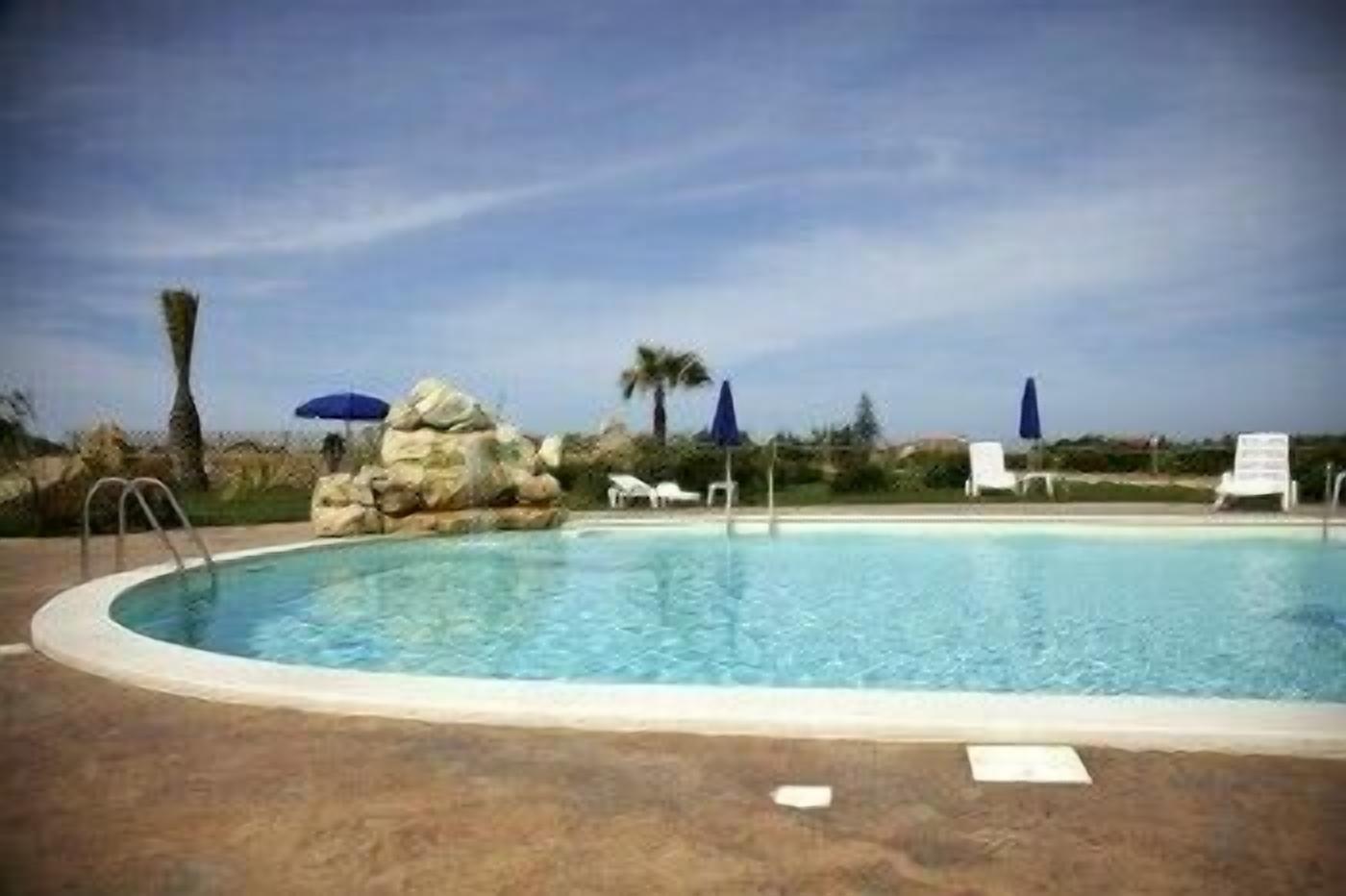 A swimming pool with lounge chairs and umbrellas, surrounded by rocks and palm trees.