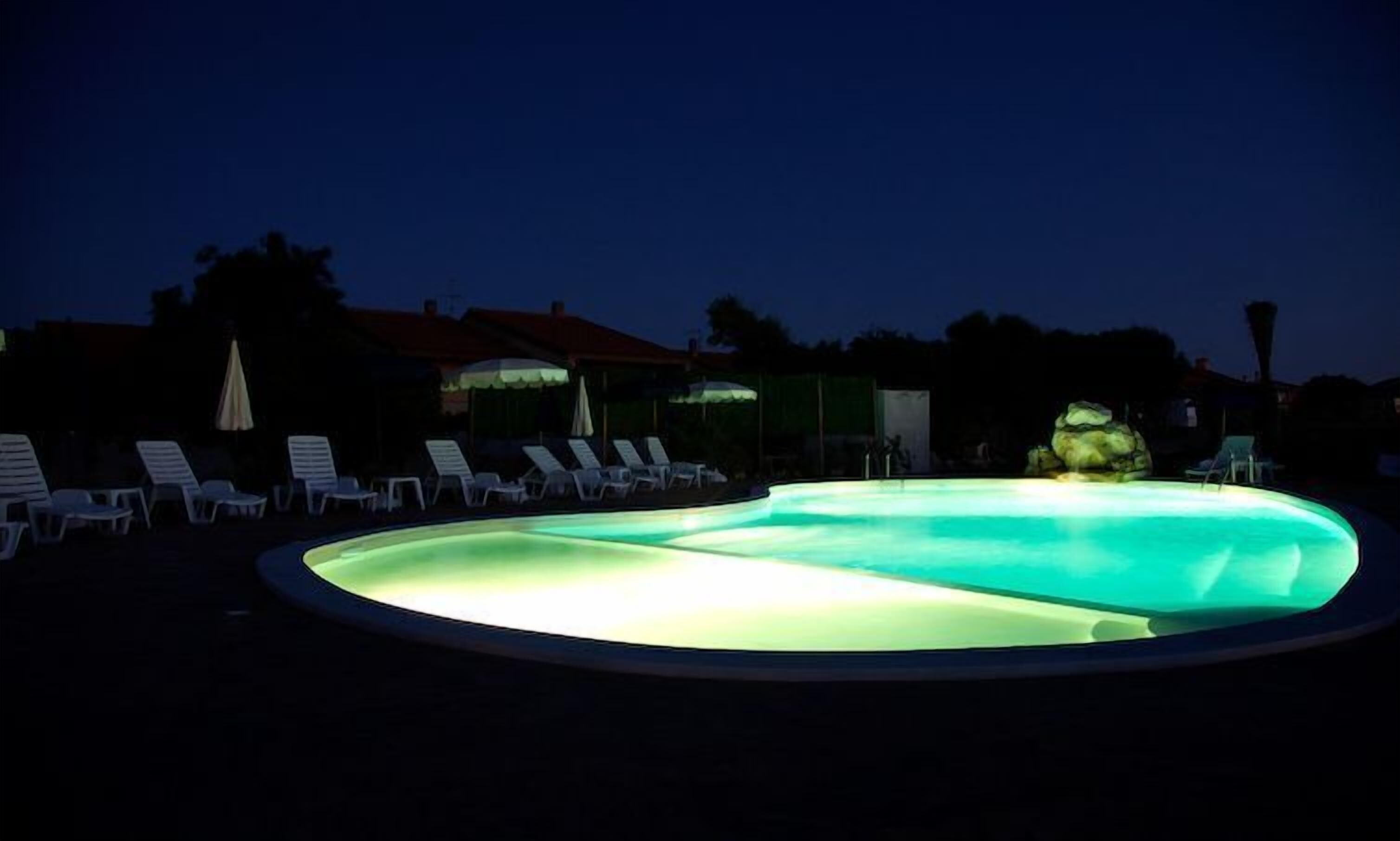 A swimming pool at dusk with lounge chairs and umbrellas around it.