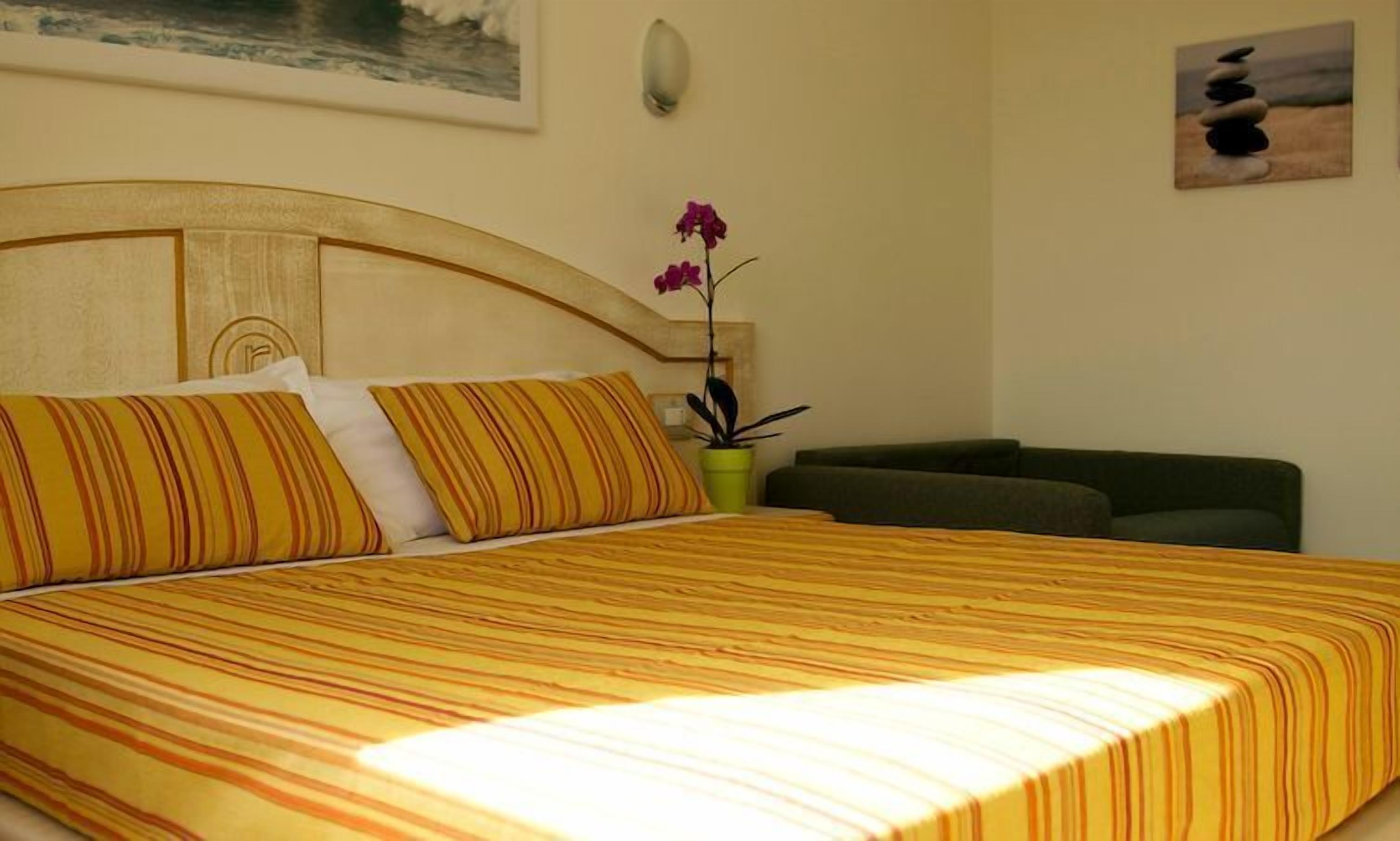 Una cama con ropa de cama a rayas, una planta verde y un cuadro en la pared.