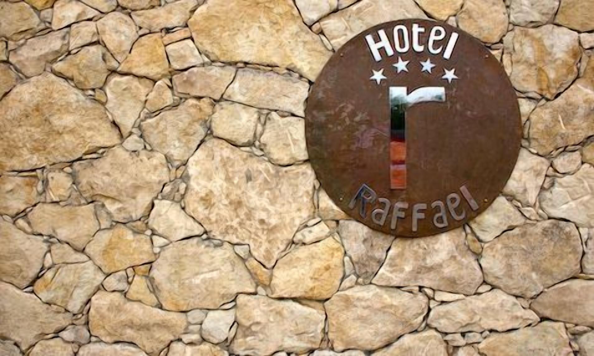 A round, metal plaque with the inscription "Hotel Raffel" on a stone wall.