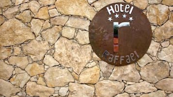 Placa redonda de metal com a inscrição 'Hotel Raffel' numa parede de pedra.