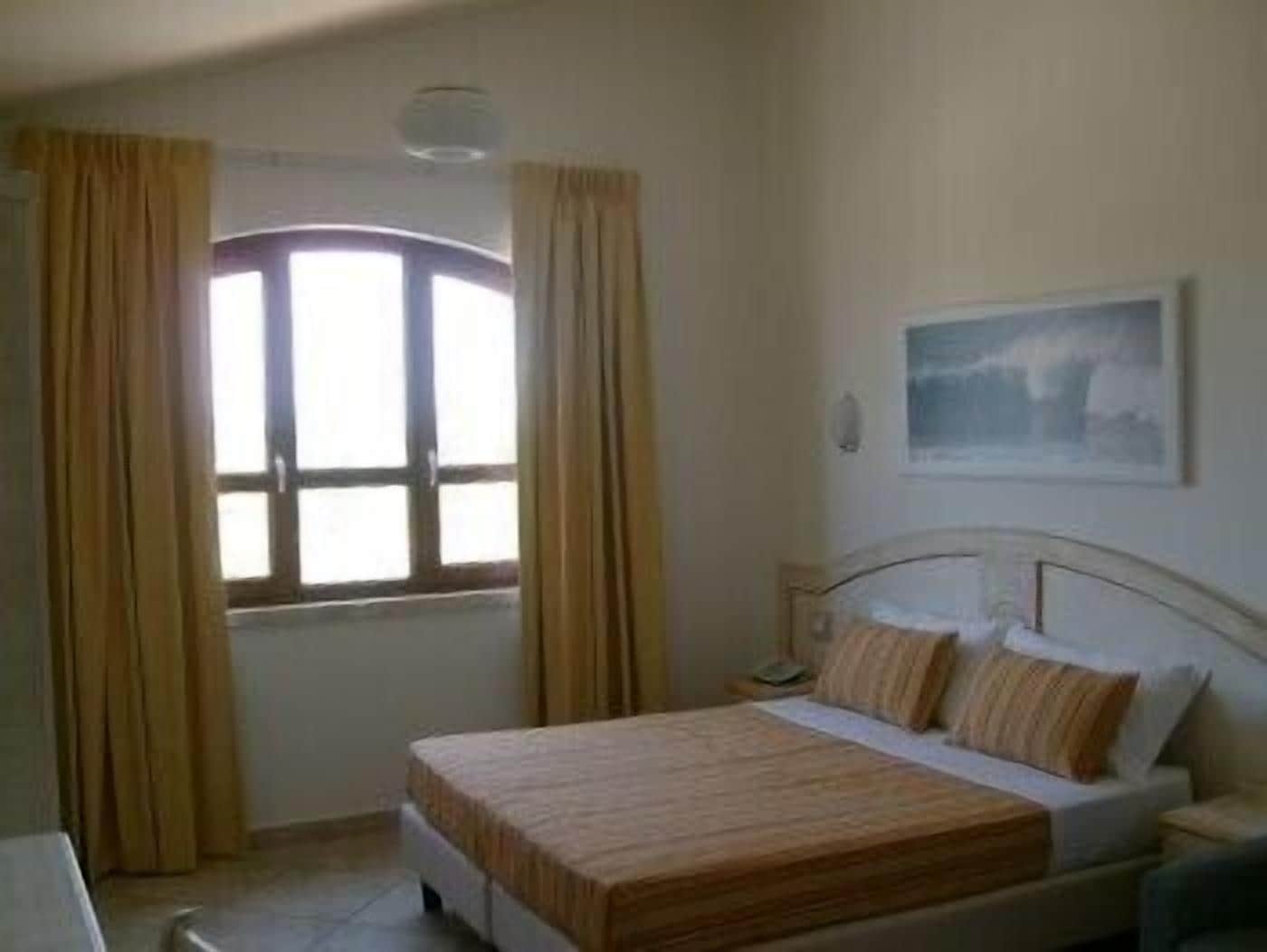A bedroom with a bed, a nightstand, a window with curtains, and a painting on the wall.