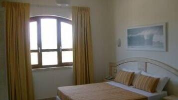 A bedroom with a bed, a nightstand, a window with curtains, and a painting on the wall.