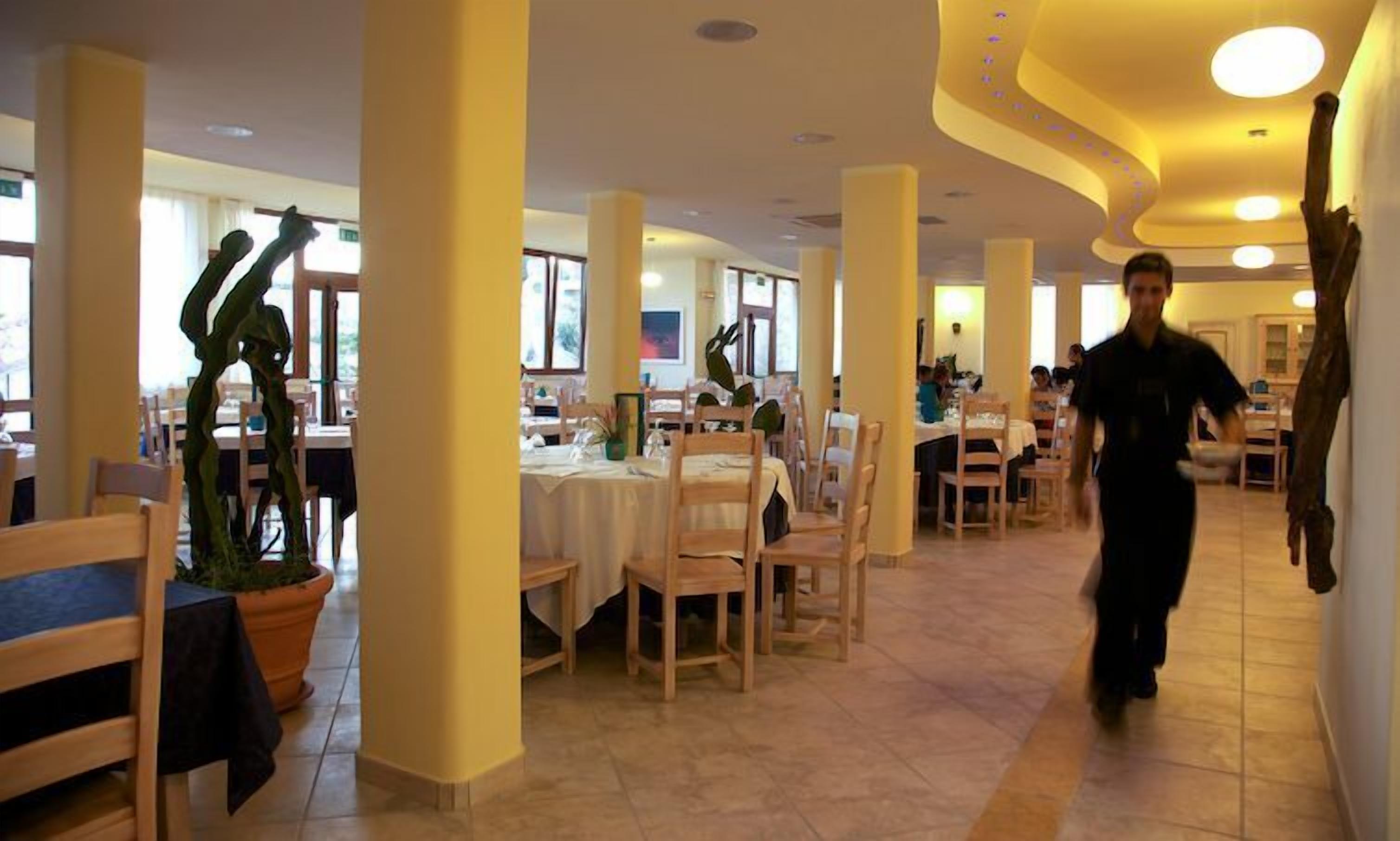 A spacious dining area with multiple tables and chairs, large pillars, and a person walking through the space.