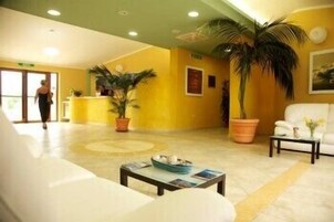 Un vestíbulo de hotel con mostrador de recepción, un sofá blanco, una mesa de centro con revistas y plantas en macetas.