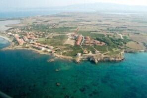 An aerial view of a coastal area with a mix of natural and developed land, including clear blue waters, rocky outcrops, and a network of paths or roads. - Hotel Raffael (San Vero Milis)