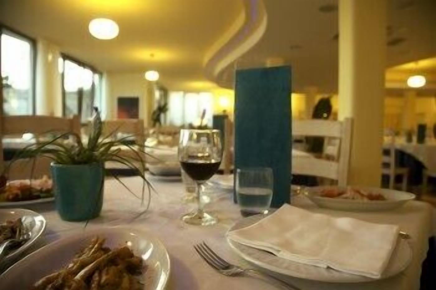 A dining area with tables set for meals, glasses of wine, and a potted plant.