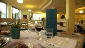 A dining area with tables set for meals, glasses of wine, and a potted plant.