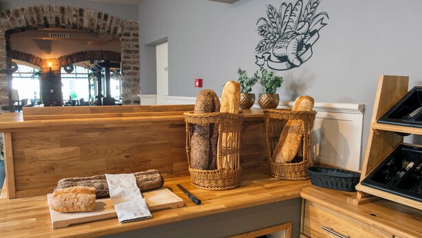 A bakery counter with bread baskets, a cutting board, a knife, and a wall-mounted plant. - Hotel Arcen (Arcen)