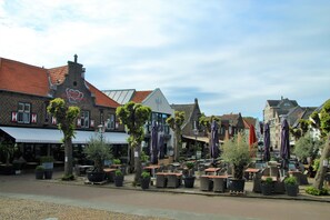 A cobblestone street with outdoor seating areas, potted plants, and a variety of buildings with distinct architectural styles. - Hotel Arcen (Arcen)