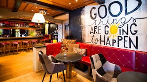 A cozy bar area with red seating, a round table, and a wall with a motivational quote. - Raffl´s Tyrol Hotel (Sankt Anton am Arlberg)
