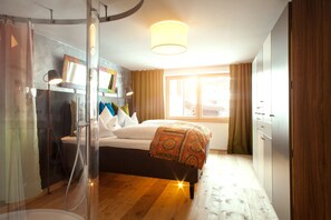 A bedroom with a bed, a shower, a wardrobe, and a window with curtains. - Raffl´s Tyrol Hotel (Sankt Anton am Arlberg)