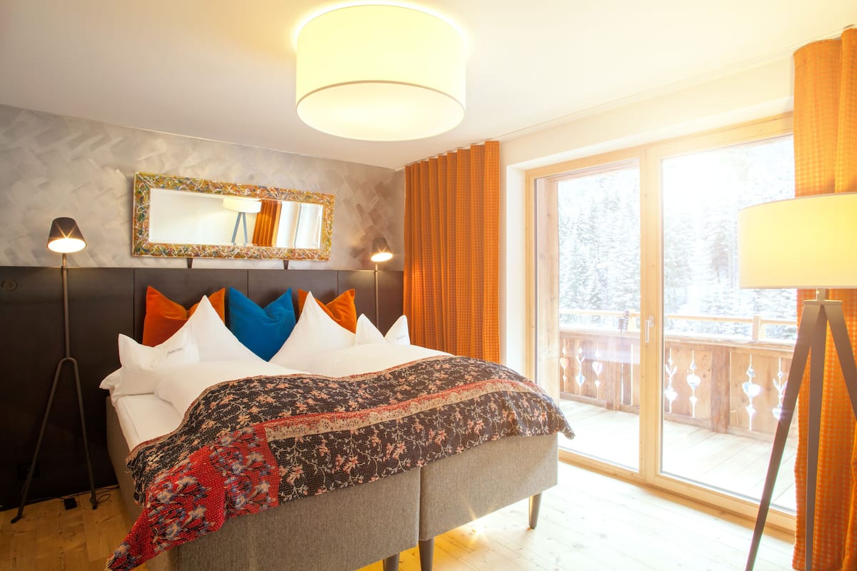 A bedroom with a bed, a large window, a mirror, and a lamp.