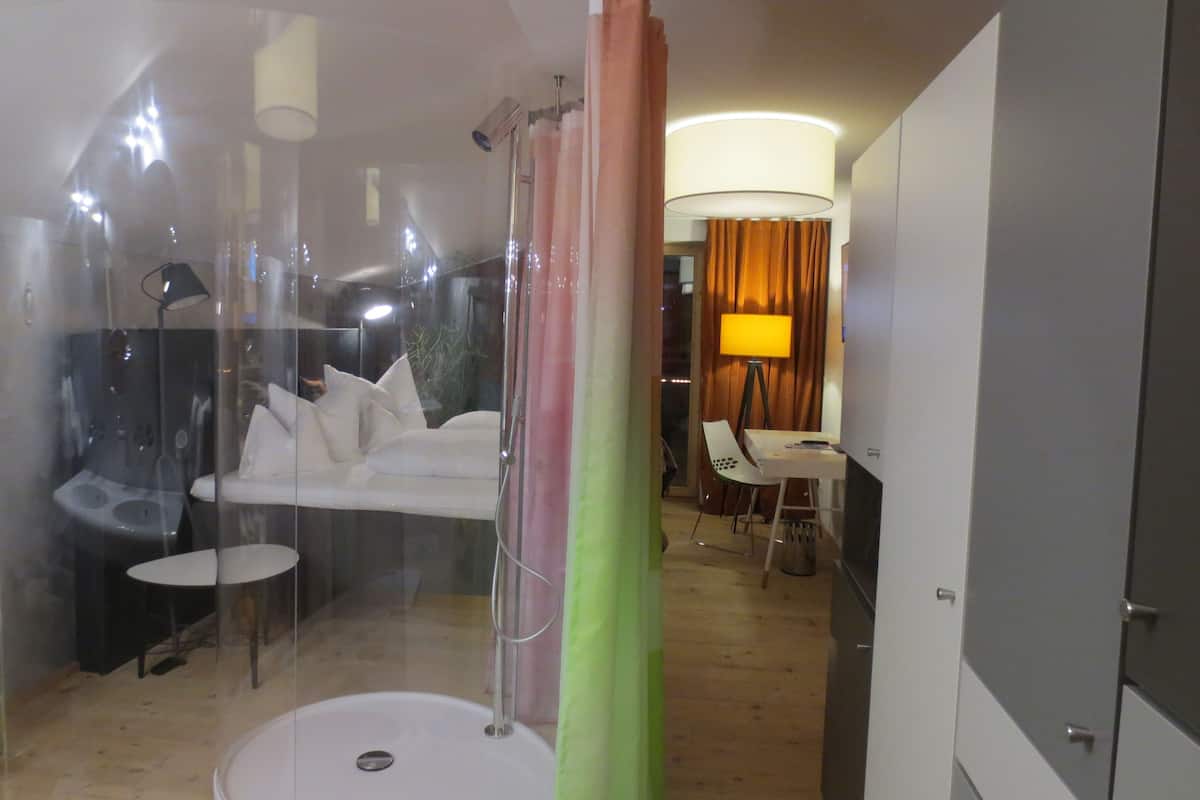 A modern bathroom with a glass shower enclosure, a white toilet, and a small table with a chair.