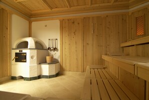 A sauna room with wooden walls, a bench, and a sauna with a control panel. - Raffl´s Tyrol Hotel (Sankt Anton am Arlberg)