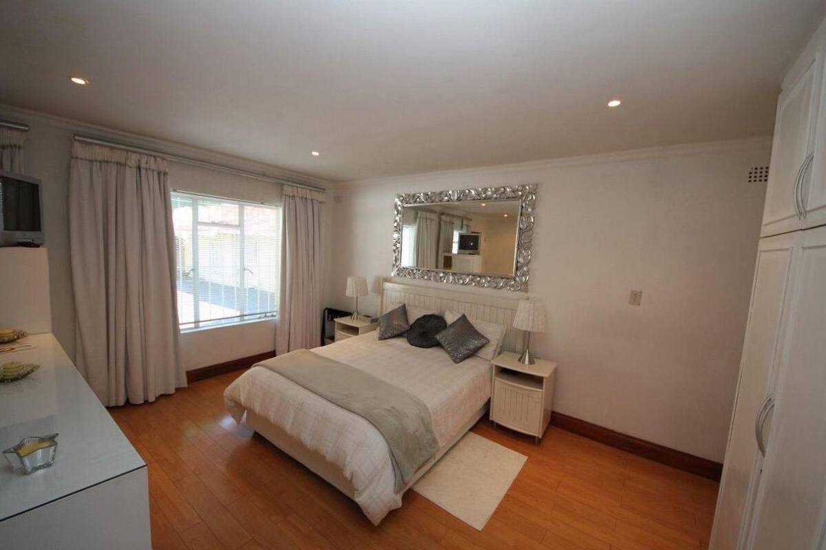 Een slaapkamer met een bed, nachtkastjes, een spiegel en een raam met gordijnen.