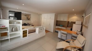 A modern kitchen with white cabinets, a dining area with a wooden table and chairs, and a built-in seating area with a sofa and armchairs. - The Munday Bed & Breakfast (Germiston)