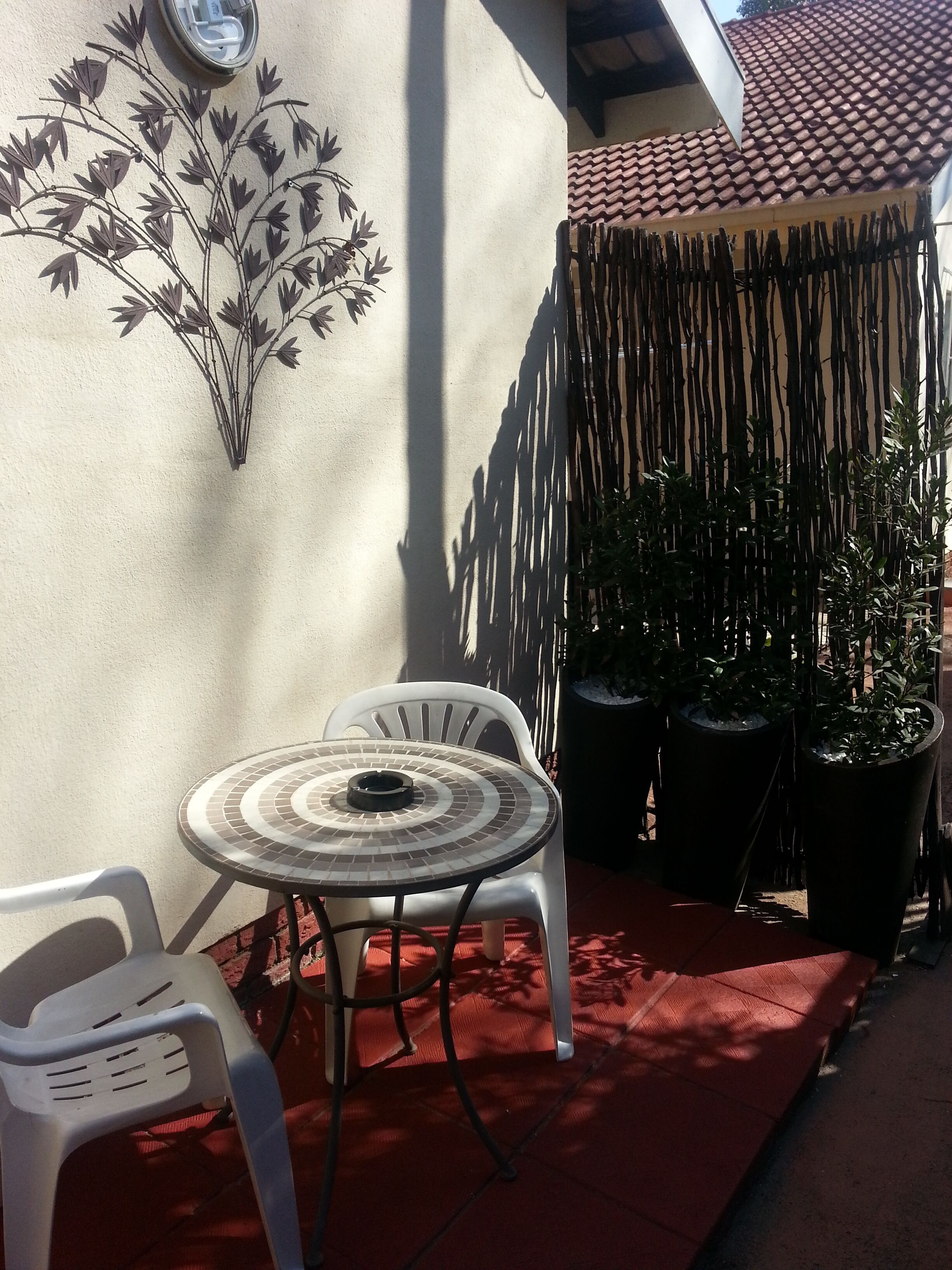 A patio with a round table and two chairs, a decorative wall, and a tiled roof.