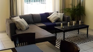 A modern living room with a sectional sofa, a coffee table, and a striped rug. - The Munday Bed & Breakfast (Germiston)