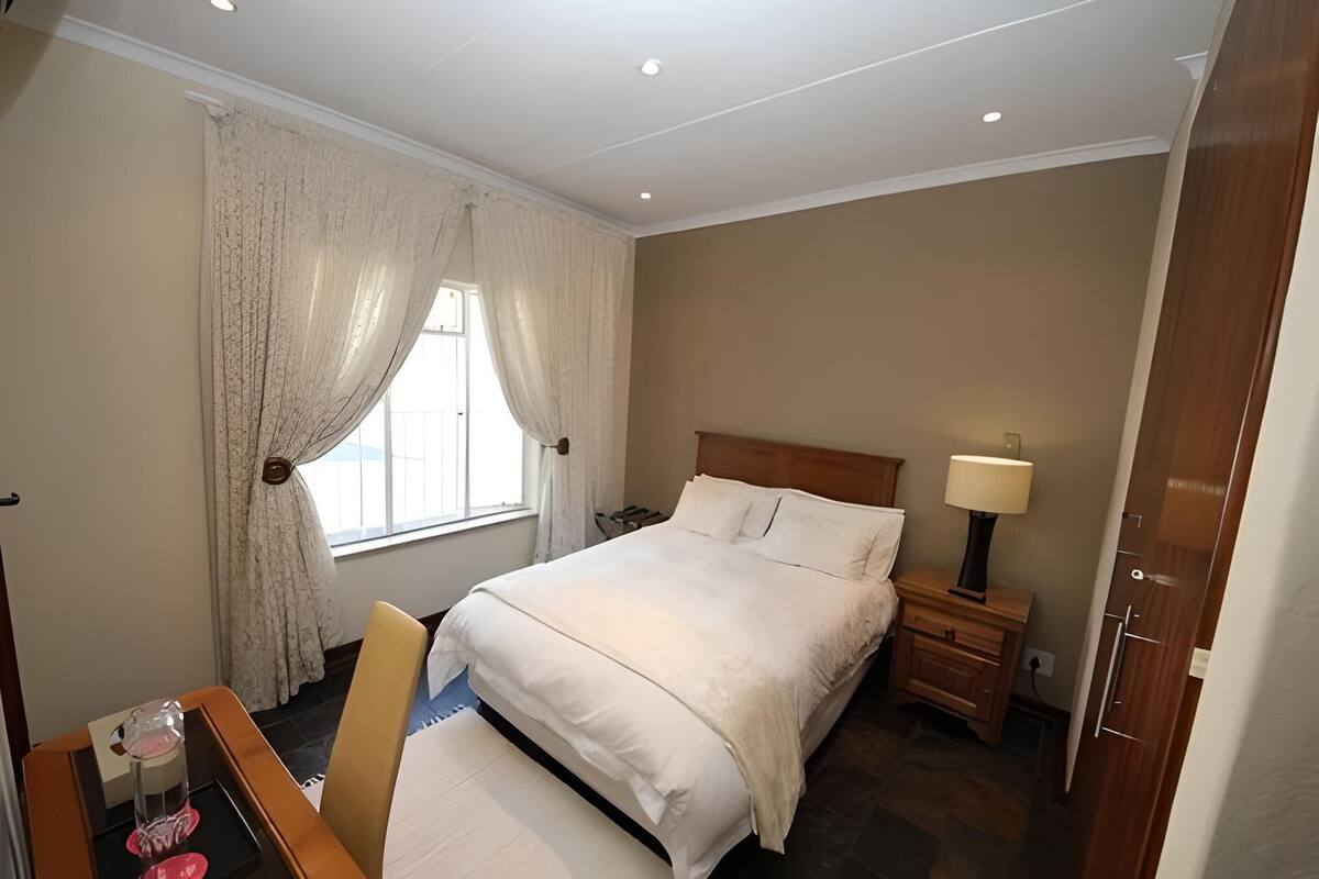 Een hotelkamer met een bed, nachtkastje, lamp, stoel en een raam met gordijnen.