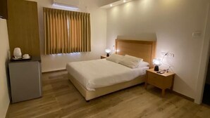 A modern bedroom with a wooden floor, a bed with white linens, a bedside table with a lamp, and a small desk with a lamp. - Berger Ultra Orthodox Hotel (Tiberias)