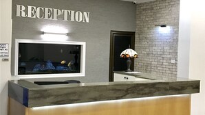 A reception desk with a marble top, a sign above it reading "RECEPTION", and a wall-mounted lamp to the right. - Berger Ultra Orthodox Hotel (Tiberias)
