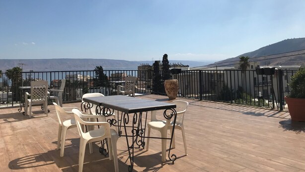 A terrace with a table and chairs, a potted plant, and a view of the sea and mountains. - Berger Ultra Orthodox Hotel (Tiberias)
