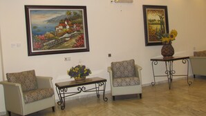 A room with two armchairs, a small table with a vase of flowers, and two framed paintings on the wall. - Berger Ultra Orthodox Hotel (Tiberias)
