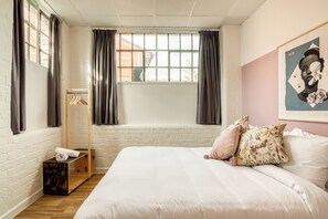 Un dormitorio con una cama grande, un banco de madera, un perchero y una ventana con cortinas.