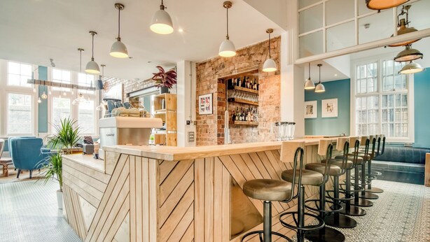 A bar area with a wooden counter, bar stools, and hanging pendant lights. - Malacuna Birmingham (Birmingham)
