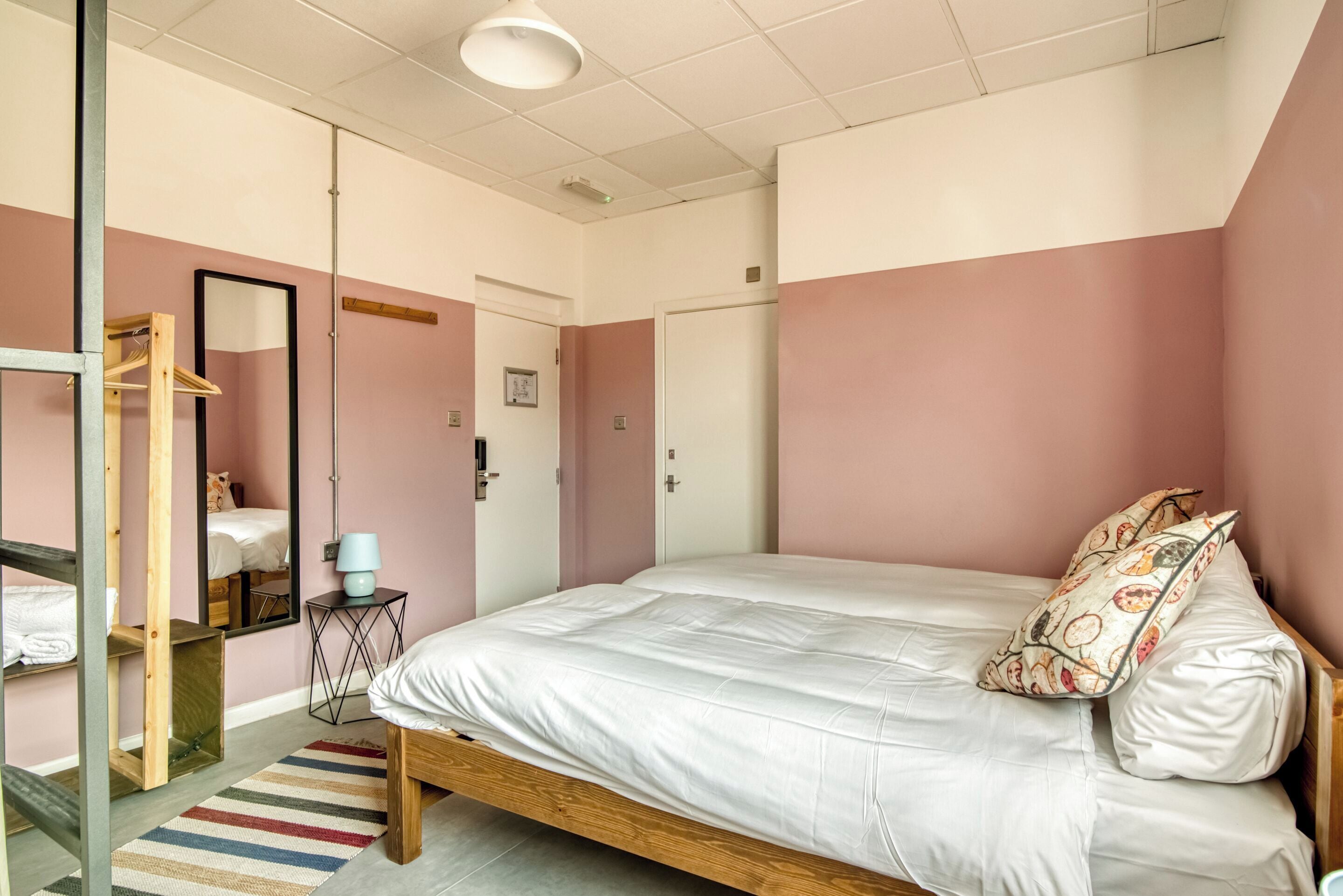 Een slaapkamer met een groot bed, een houten kledingkast, een spiegel en een klein tafeltje met een lamp.